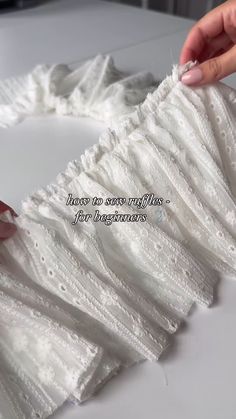 a woman is working on a piece of white lace with her hands holding the edge