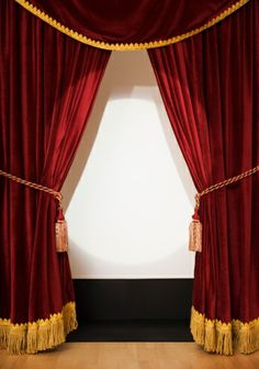 a red curtain with tassels hanging from it's sides in front of a white wall