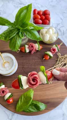 a person holding a piece of food on top of a wooden tray with tomatoes, mozzarella and spinach leaves