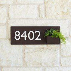 a house number sign mounted to the side of a stone wall with a plant in it