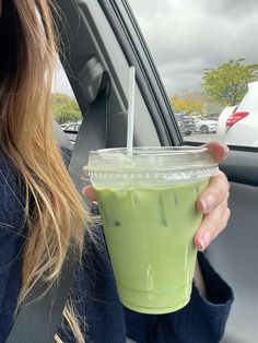 a woman is holding a green drink in her hand while sitting in the back seat of a car