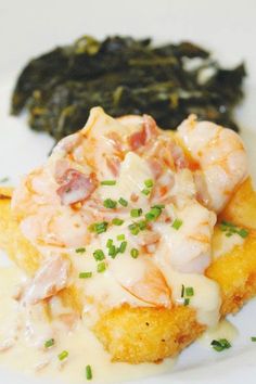 a white plate topped with shrimp and grits next to green spinach leaf covered in gravy