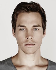 a close up of a person wearing a gray shirt and looking at the camera with a serious look on his face