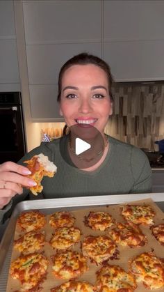 a woman holding up a pizza in front of a baking sheet with several small bites taken out of it