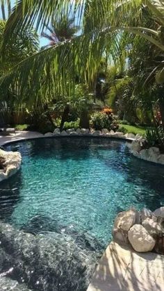 an outdoor swimming pool surrounded by palm trees and rocks with water running down the side