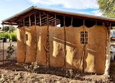 a small adobe building with wood framing and windows on the side, surrounded by dirt