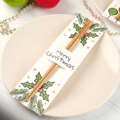 two chopsticks on a plate with merry christmas tags attached to them, sitting next to some ornaments