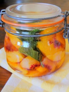 a glass jar filled with peaches and mint on top of a yellow checkered napkin