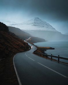 an empty road on the side of a mountain with snow covered mountains in the background