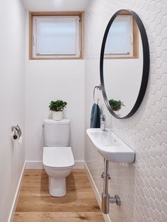 a white toilet sitting next to a bathroom sink under a round mirror on a wall