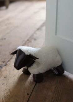 a stuffed sheep sitting on the floor next to an open door with it's head sticking out