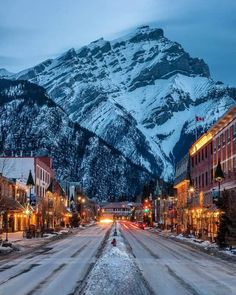 a snowy mountain is in the distance with buildings on both sides and street lights lit up at night