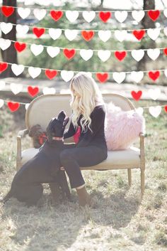 a woman sitting on top of a bench next to a dog in front of a string of hearts