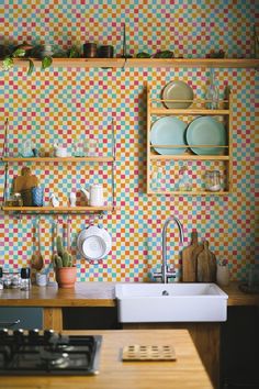 a kitchen with colorful tiles on the wall and shelves above the sink, next to a stove