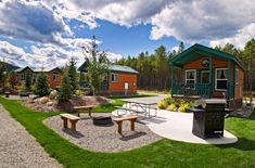 an outdoor grill area with picnic tables and bbqs next to cabins in the woods