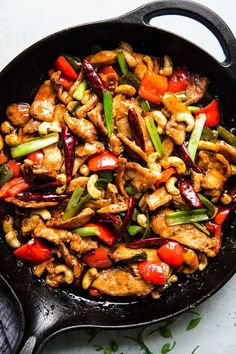 a skillet filled with chicken, peppers and cashews on top of a table