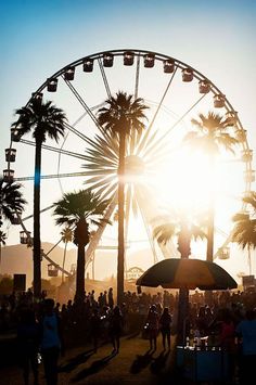 a ferris wheel with palm trees in the foreground and people walking around at sunset