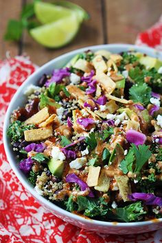 a white bowl filled with salad on top of a red and white table cloth next to lime wedges