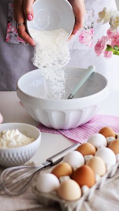 a person pouring flour into a bowl next to eggs