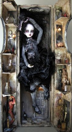 a doll in a box with shelves and mirrors behind her is wearing a black dress