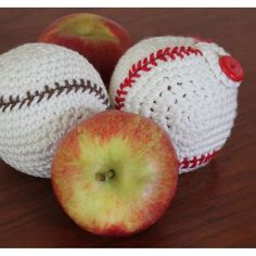 three apples and two crocheted baseballs sitting on a wooden table with one apple cut in half