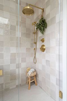 a bathroom with tiled walls and a wooden stool in the shower area, along with a gold faucet