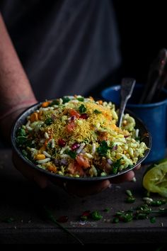 a person holding a bowl filled with food next to a knife and some lime wedges