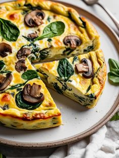 a quiche with spinach, cheese and mushrooms on a plate next to a fork