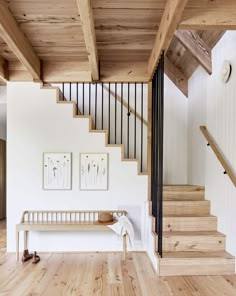 a wooden bench sitting under a stair case next to a set of wood stairs in a white room