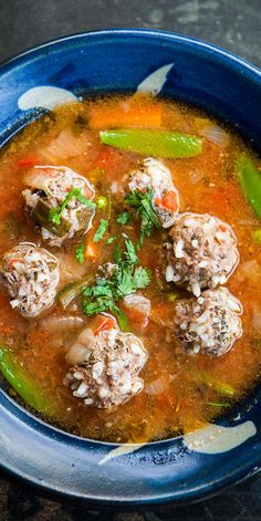 a blue bowl filled with meatball soup on top of a wooden table next to a spoon