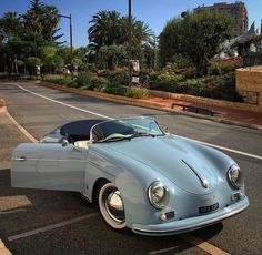 an old blue car parked on the side of the road in front of some palm trees