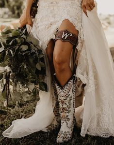 a woman in cowboy boots is sitting on the ground with her legs crossed and holding flowers