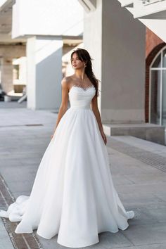 a woman in a white wedding dress standing on the sidewalk