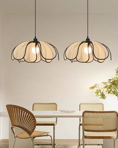 three lights hanging over a dining table with chairs and a potted plant in the corner