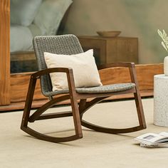 a rocking chair sitting on top of a carpeted floor next to a white vase