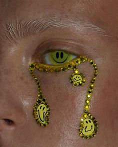 a man's face with smiley faces painted on his eyes and gold beads around the eyes