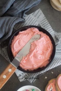 a pan filled with pink frosted doughnuts next to a knife and bowl of sprinkles