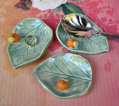 three leaf shaped dishes with spoons and flowers in the background on a pink tablecloth