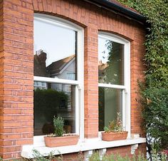 a cat sitting on the window sill in front of a brick building with potted plants