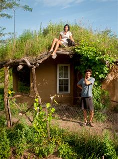 two people are sitting on the roof of a small house with grass growing on it