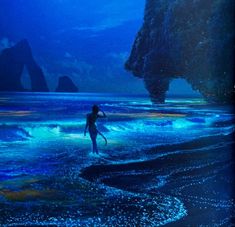 a person is walking in the water near rocks and cliffs at night with blue lights