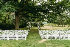 an outdoor ceremony set up with white chairs and greenery on the aisle, surrounded by trees