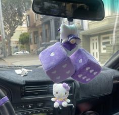 a hello kitty stuffed toy hanging from the dashboard of a car with two purple dices attached to it