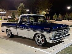 an old blue and white truck parked in a parking lot next to some buildings at night