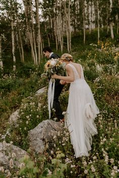 a bride and groom walking through the woods with wildflowers on their wedding day