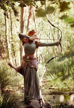 a woman with red hair is holding an arrow in the woods