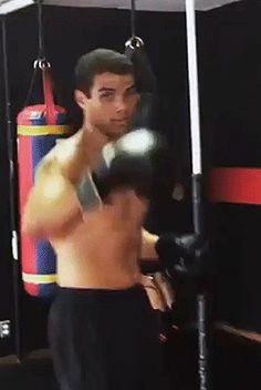 a man standing in a boxing ring wearing black shorts and holding a punching mitt