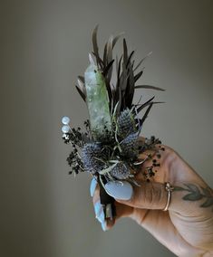 a person's hand holding a flower arrangement in their left hand with other flowers on it