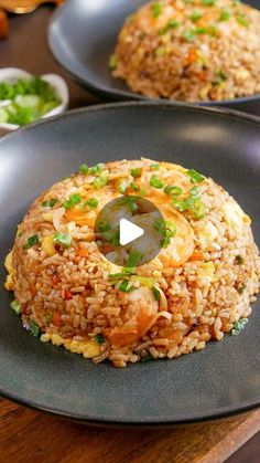 two black plates filled with rice and vegetables on top of a wooden table next to other dishes