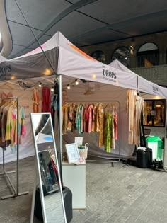 an open tent with clothes on display in front of it and a mirror next to it